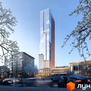 Високий скляний хмарочос THE ONE з коричневими елементами фасаду в зимовому міському пейзажі. Навколо засніжені дерева, вулиця з автомобілями та комерційні будівлі.