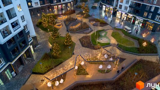 Житловий комплекс Синергія Сіті з житловими будинками, комерційними приміщеннями на першому поверсі та святково освітленим двором з алеями, лавками та ялинками.
