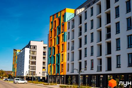 Житловий комплекс Квартал Краківський. Фасади будинків оздоблені яскравими кольорами: жовтим, помаранчевим та бірюзовим. Поруч розташована дорога з припаркованими автомобілями.