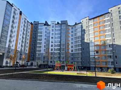 Багатоповерхові будинки Житлового комплексу Квартал Галицький з сірими, білими та помаранчевими фасадами. Прибудинкова територія включає дитячий майданчик та зелені зони.