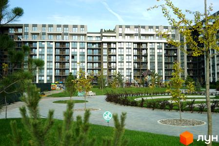 Новобудова ЖК PARK LAND з фасадами з сірої та білої плитки, численними балконами та панорамними вікнами. Прибудинкова територія з зеленими газонами, деревами та дитячим майданчиком.