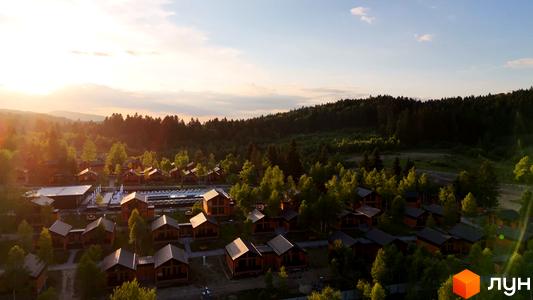 Котеджне містечко KM PHOENIX MEDICAL RESORT з дерев'яними будиночками та басейном на фоні лісу. Територія комплексу оточена зеленню та деревами.