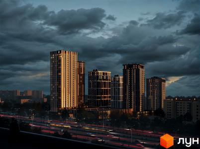 Житловий комплекс Avalon Up у вечірньому світлі. Сучасні висотні будинки з підсвіченими вікнами, розташовані вздовж жвавої дороги з автомобільним трафіком.