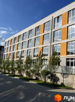 Багатоповерховий будинок ЖК Sanville Park з великими вікнами та помаранчевими вставками на фасаді. Перед будинком доглянута прибудинкова територія з деревами та газоном.