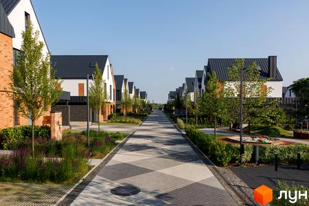 Котеджне містечко LAGOM: ряд білих будинків з темними дахами та доглянутою територією з алеєю та дитячим майданчиком.