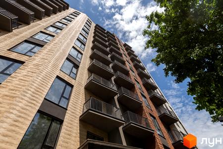 Апарт-комплекс Ітака з цегляним фасадом та балконами на фоні блакитного неба з хмарами. Будинок має багато вікон та виступаючі балкони.