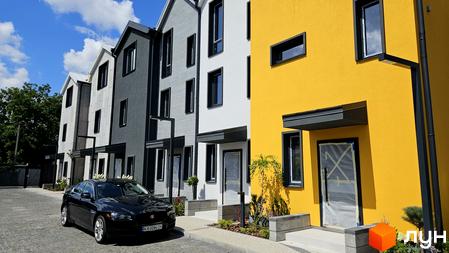 Таунхауси New Smart 9: фасади будинків у сірих та жовтих кольорах, з чорними вікнами, перед будинками розташована бруківка та зелені насадження.