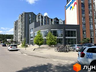 Зовнішній вигляд житлового комплексу Scandia з багаторівневими фасадами та панорамними вікнами. На прибудинковій території розташовані дерева та парковка з велосипедами.