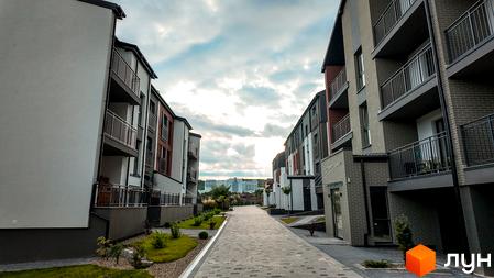 Житловий комплекс Вілла Швейцарія. Сучасні будівлі з балконами та бруківкою, що веде до них. Навколо зелені насадження та дерева.