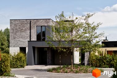 Котеджне містечко О.Краса: двоповерховий будинок з цегляним фасадом та великими вікнами, оточений зеленню та деревами. Прибудинкова територія з бруківки та ландшафтного дизайну.