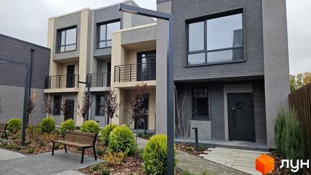 Зовнішній вигляд таунхаусів Sвій Dім 2 з сірого та бежевого цегли, з великими вікнами та балконами. Навколо будинку зелені насадження та лавки.