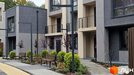 Зображення таунхаусів Sвій Dім 2 з сірого цегли, з балконами та лавками на прибудинковій території.