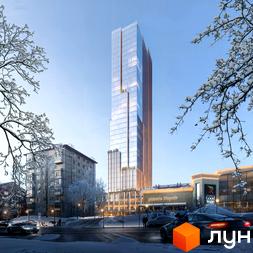 Високий скляний хмарочос THE ONE з коричневими елементами фасаду в зимовому міському пейзажі. Навколо засніжені дерева, вулиця з автомобілями та комерційні будівлі.