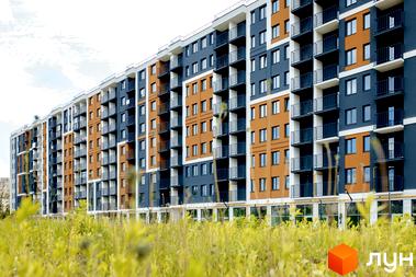 Новобудова ЖК КЕЛЬЦЕ з помаранчевими та синіми фасадами, балконами та зеленою травою на передньому плані.