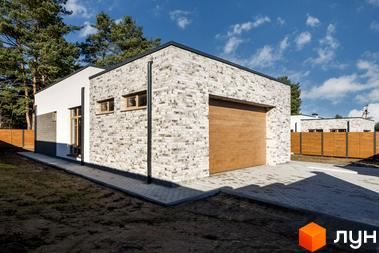 Котеджне містечко LOTUS. Зовнішній вигляд будинку з цегляним фасадом, дерев'яними вікнами та гаражними воротами. Навколо будинку вимощена бруківкою прибудинкова територія та зелена зона.