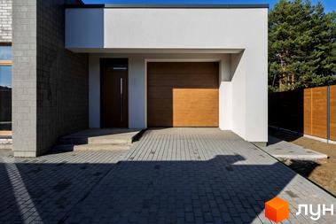 Зовнішній вигляд будинку КМ LOTUS з дерев'яними гаражними воротами та вхідними дверима. Прибудинкова територія вимощена плиткою.