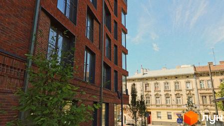 Будівля З.40 з червоної цегли з великими вікнами та балконами, перед нею зелене дерево. Навпроти розташовані старіші будинки та вулиця.