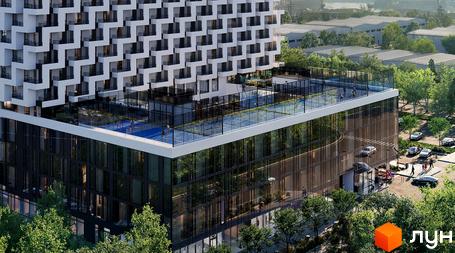 Апарт-готель Circle з білою фасадною обробкою та скляними елементами, що має відкритий басейн та спортивні майданчики на даху. Навколо будівлі розташовані дерева та паркувальні місця.