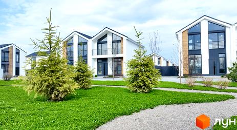 Котеджне містечко КМ Gardd House Eco Village. Зовнішній вигляд будинків з великими вікнами та прибудинкова територія з зеленим газоном та деревами.