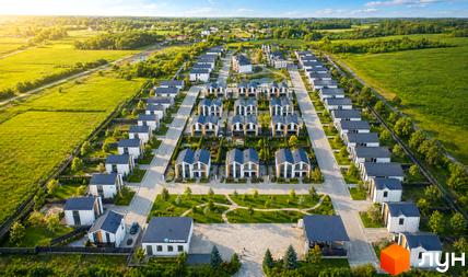 Котеджне містечко Gardd House Eco Village з білими будинками та синіми дахами, розташоване серед зелених полів та дерев.