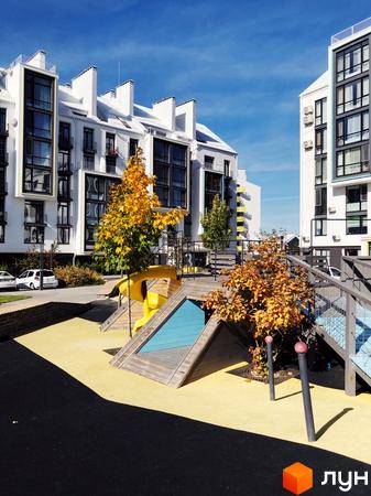 Житловий комплекс City Lake: білі багатоповерхові будинки з великими вікнами та балконами. На передньому плані дитячий майданчик з жовтим покриттям та осінніми деревами.