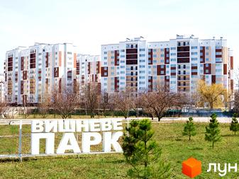 Житловий комплекс Сади Вишневі: багатоповерхові будинки з білими та коричневими фасадами, балконами та великою кількістю вікон. Поруч зелена зона з молодими деревами та написом 