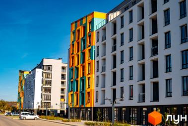 Житловий комплекс Квартал Краківський. Фасади будинків оздоблені яскравими кольорами: жовтим, помаранчевим та бірюзовим. Поруч розташована дорога з припаркованими автомобілями.