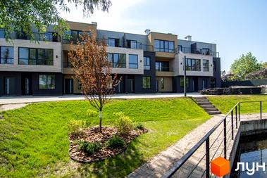 Зовнішній вигляд таунхаусів Rusaniv Gardens з великими вікнами та балконами. На території комплексу газон, доріжки та декоративні дерева.