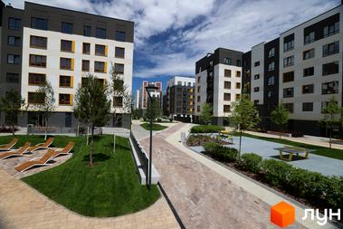 Житловий комплекс Молодість: фасади будинків з білими та сірими елементами, жовтими вікнами, зелена прибудинкова територія з лежаками та столами для настільного тенісу.