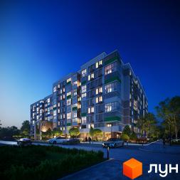 Багатоповерховий будинок ЖК Литовський квартал з великими вікнами та підсвічуванням у вечірню пору. На території є парковка та зелені насадження.